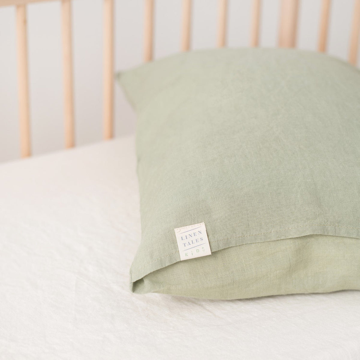 2. Sage green linen pillowcase with Linen Tales label on a white bed