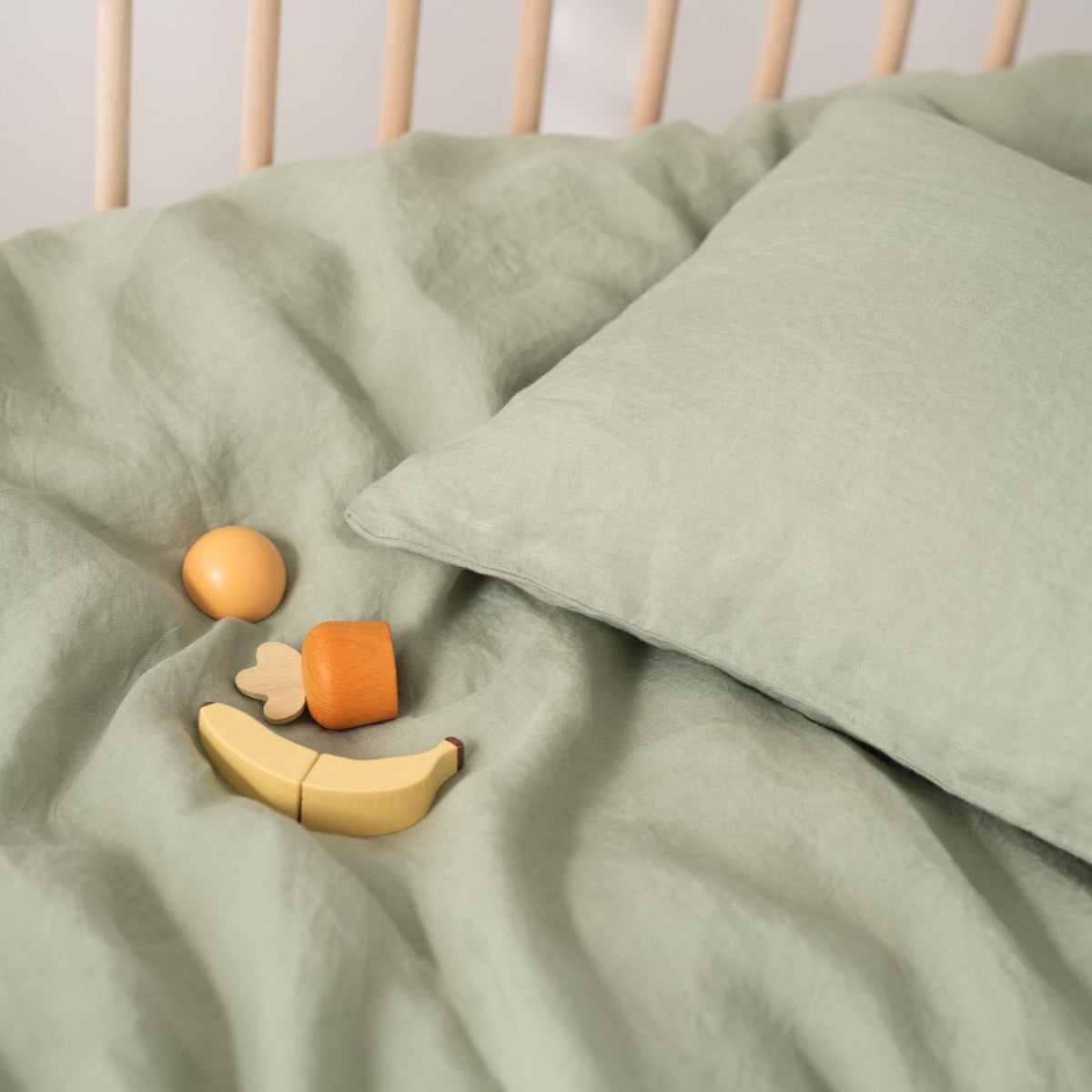 11. Sage green linen duvet cover with pillowcase and wooden toys on crib