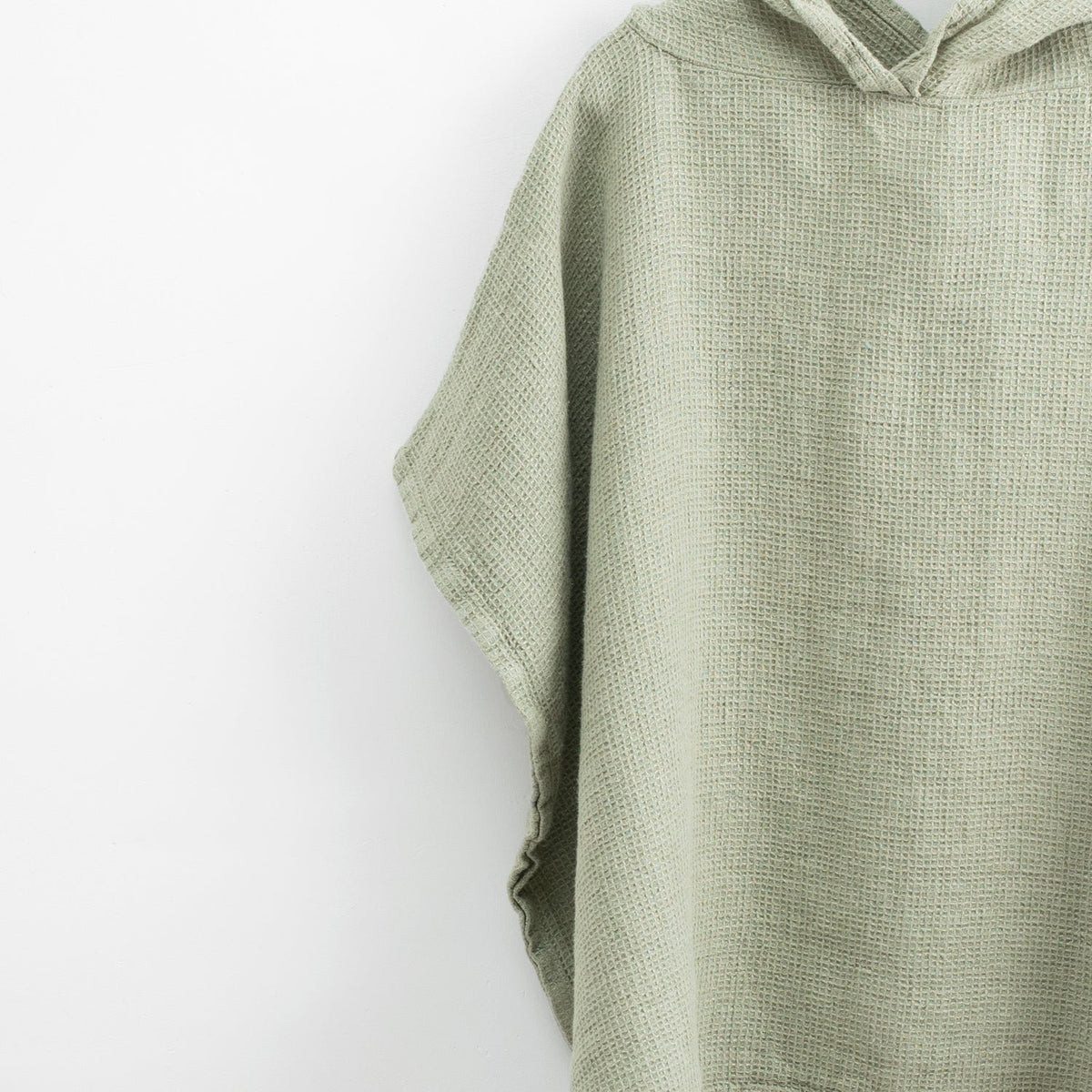 3. Close-up of sage green linen poncho showing fine waffle texture and hood detail