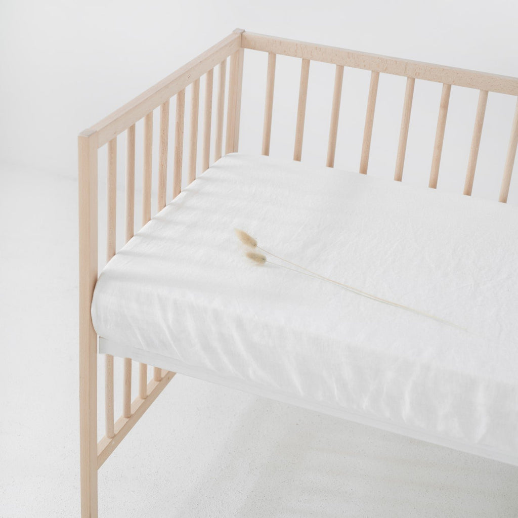 1. White linen fitted sheet on a wooden crib with a minimalistic design, showcasing the soft texture and elastic hem