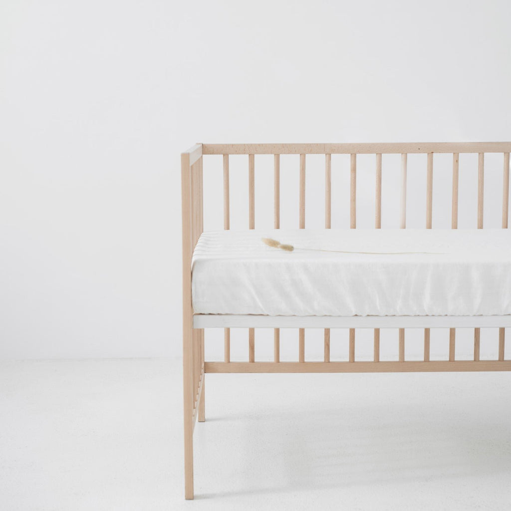 4. White linen fitted sheet on a wooden crib in a bright room, emphasizing the sheet's fit and texture