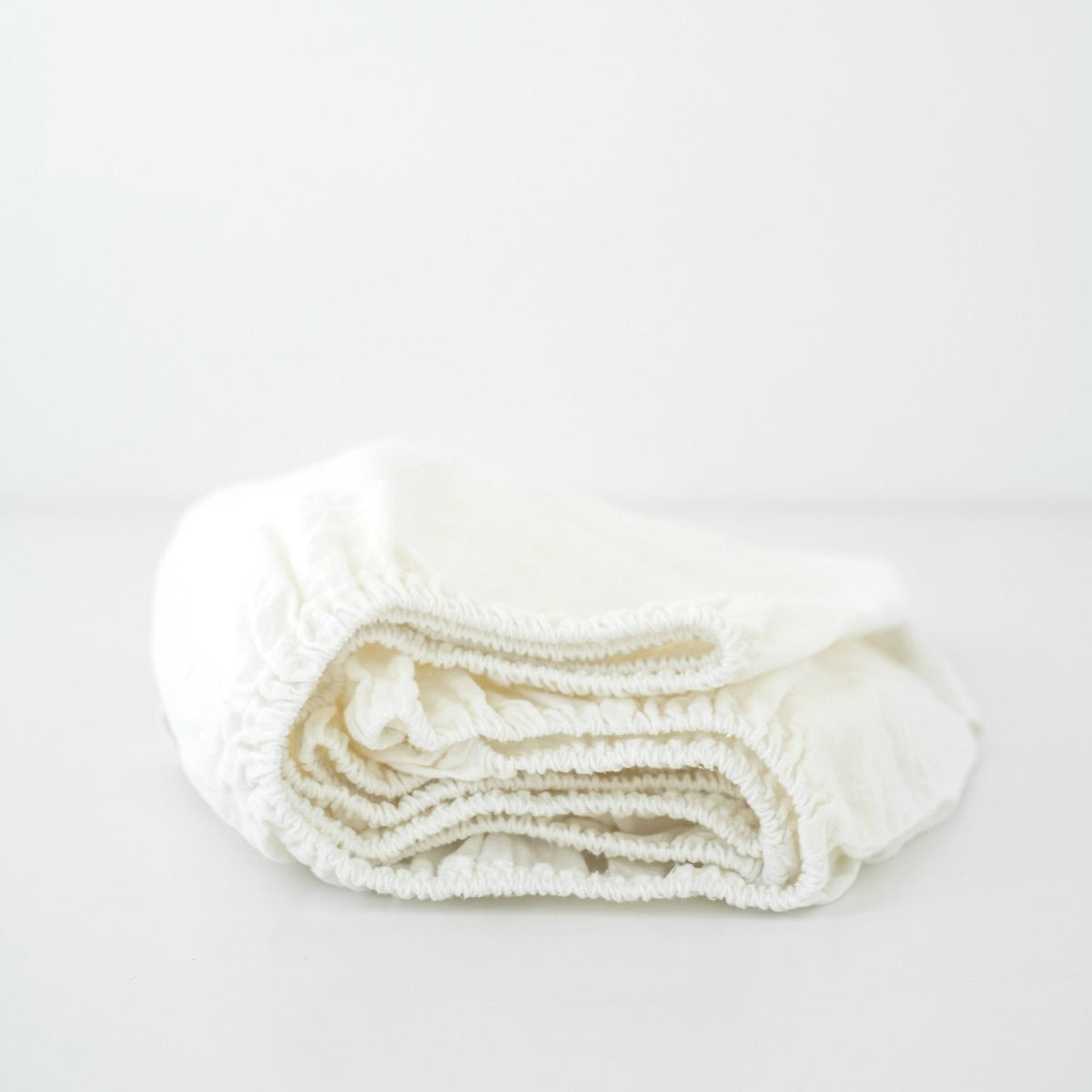 3. Folded white linen fitted sheet on a plain background, showing elastic hem and soft material