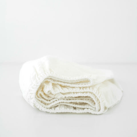 3. Folded white linen fitted sheet on a plain background, showing elastic hem and soft material