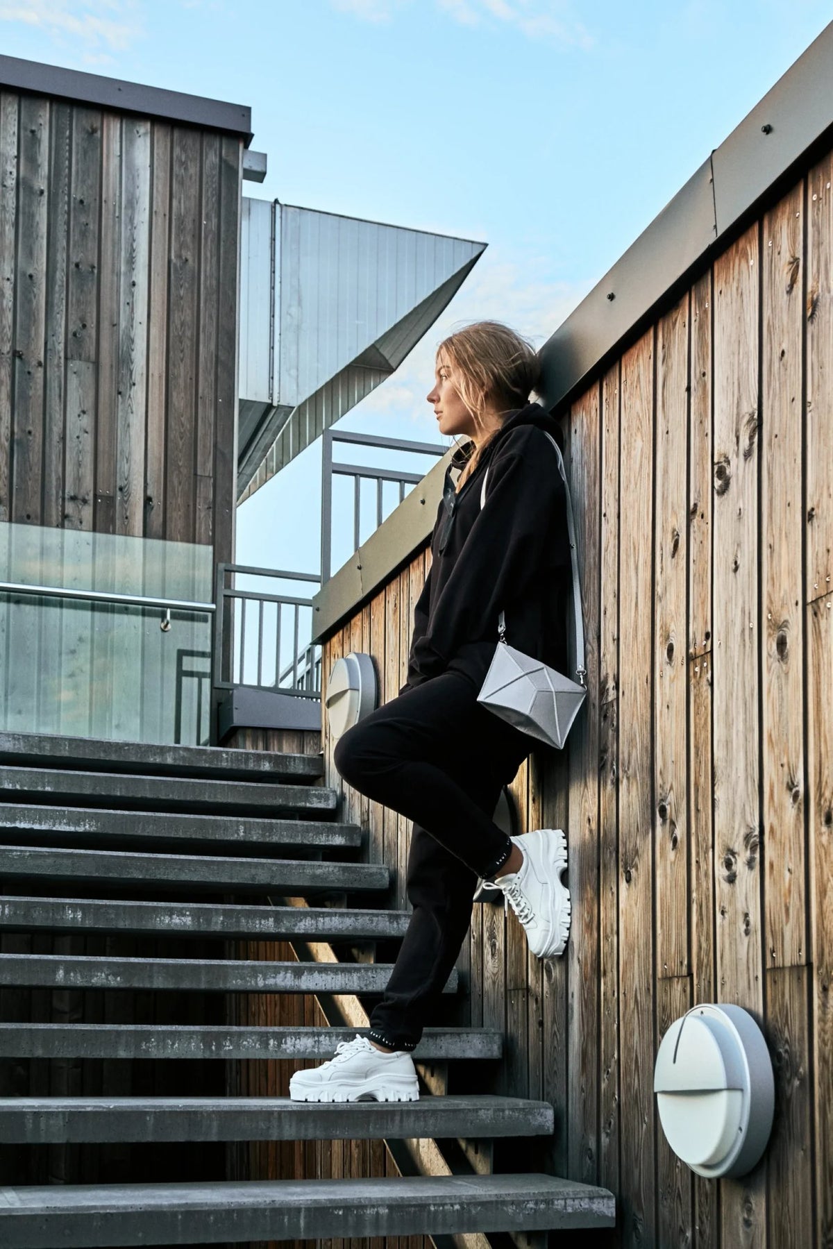 2. Women's light grey FACET Mini leather shoulder bag by Gerda Retter Design, worn with black outfit on outdoor stairs