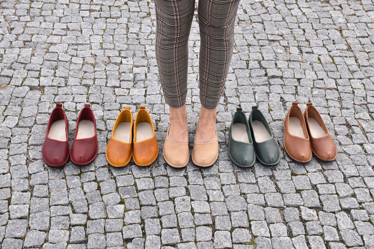 3. Woman standing on cobblestone with Omaking Kuutsid shoes in various colors, including dark green, red, and tan