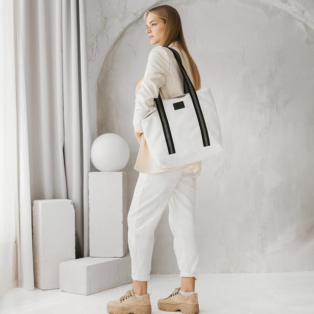 2. Woman carrying Muni white denim tote bag with black straps, styled with casual outfit