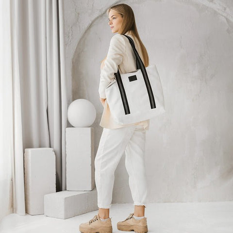 2. Woman carrying Muni white denim tote bag with black straps, styled with casual outfit