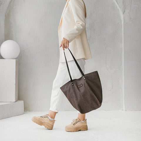 4. Side view of woman holding Muni brown denim tote bag with black leather handles in a lifestyle setting