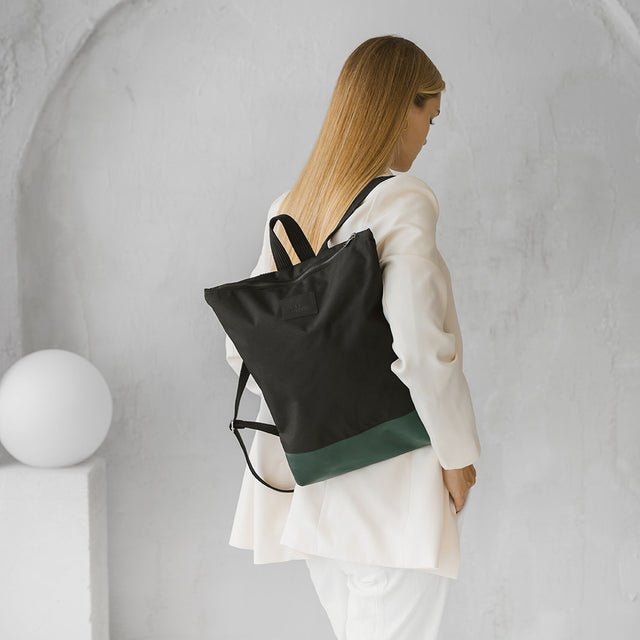 1. Woman wearing Muni waterproof backpack with green leather bottom, shown from the side in a lifestyle setting