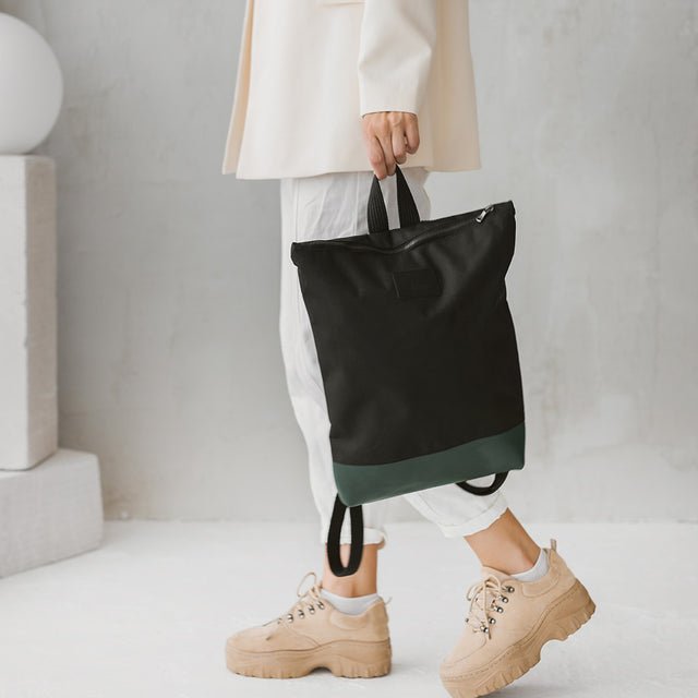 2. Muni waterproof backpack with green leather bottom held by woman, showcasing adjustable straps and zipper closure