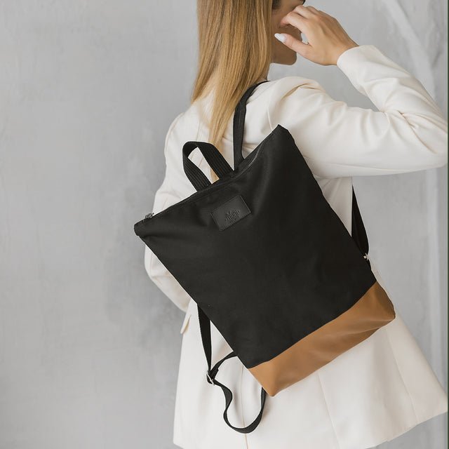 2. Woman wearing Muni waterproof backpack with tan leather bottom, styled with white blazer in lifestyle setting