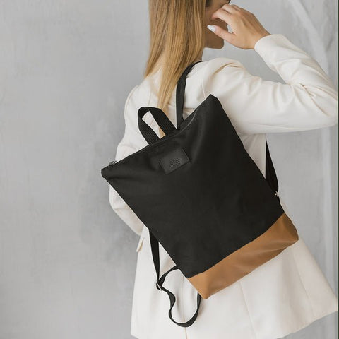 2. Woman wearing Muni waterproof backpack with tan leather bottom, styled with white blazer in lifestyle setting