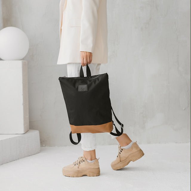 3. Woman carrying Muni waterproof backpack with tan leather bottom, paired with casual outfit in lifestyle setting