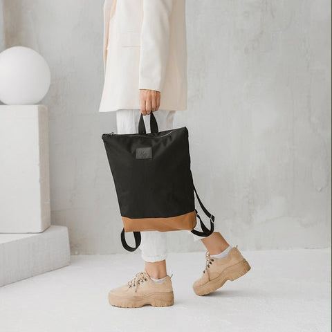 3. Woman carrying Muni waterproof backpack with tan leather bottom, paired with casual outfit in lifestyle setting