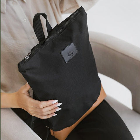 1. Woman holding Muni waterproof backpack with tan leather bottom, showcasing stylish design in lifestyle setting