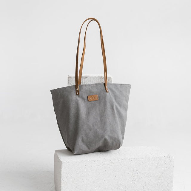 4. Studio shot of Muni grey denim tote bag with tan leather handles, displayed on white block