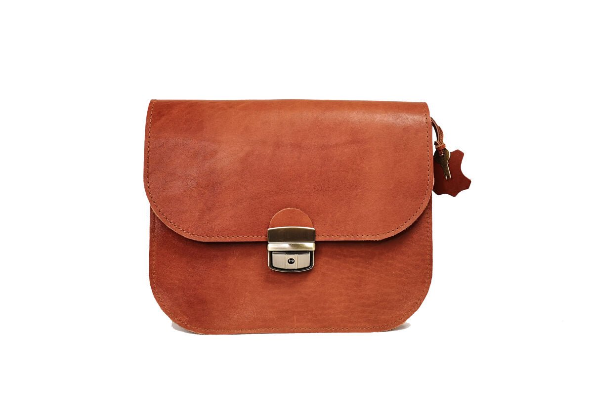 8. Front view of small Zelma Kraft natural leather saddle bag in light brown, studio setting with buckle closure