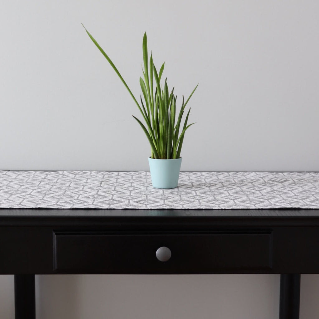 1. Table runner with Harjumaa folk art pattern in grey and white on dark wooden table with green plant in light blue pot