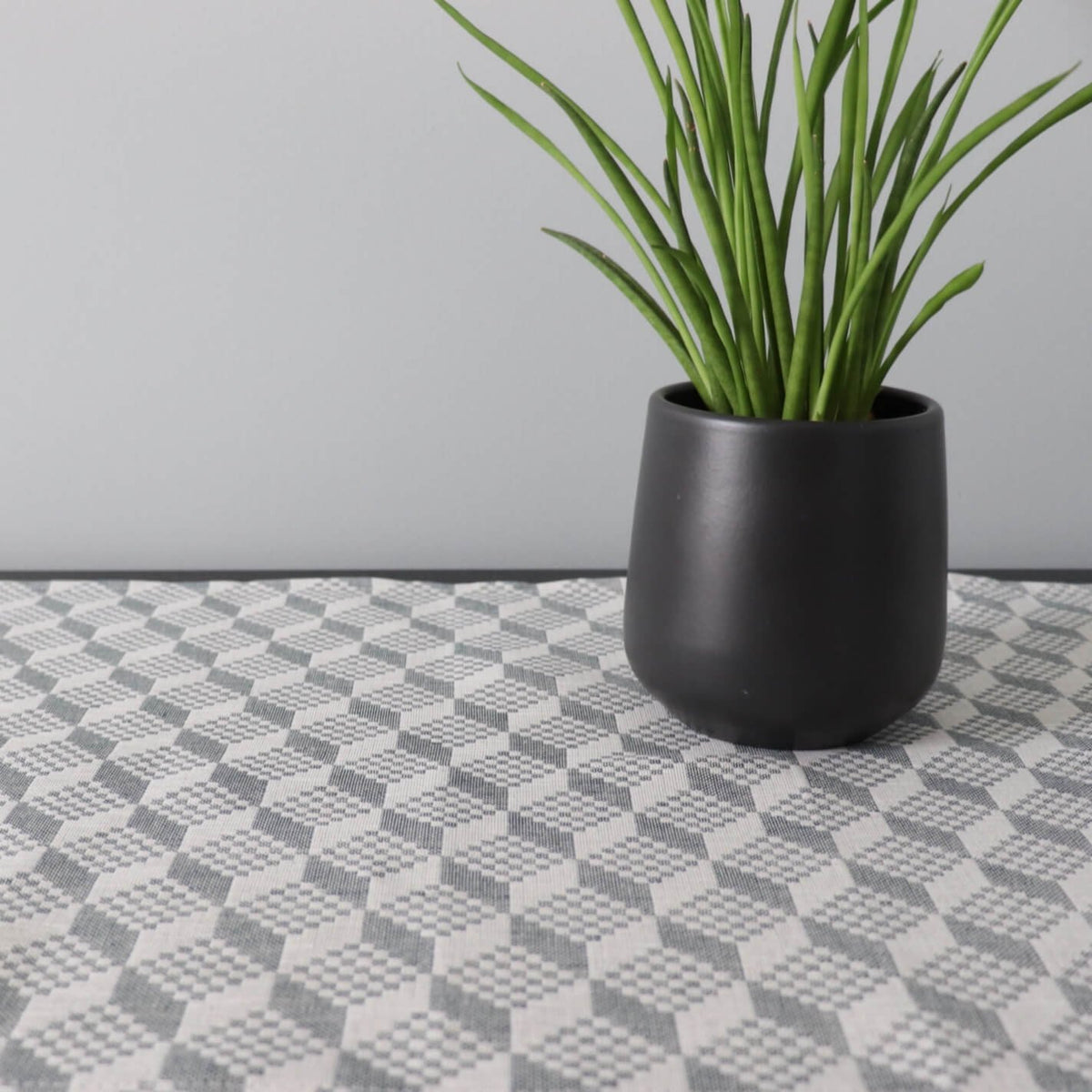 2. Table runner with Virumaa pattern under black plant pot on light background