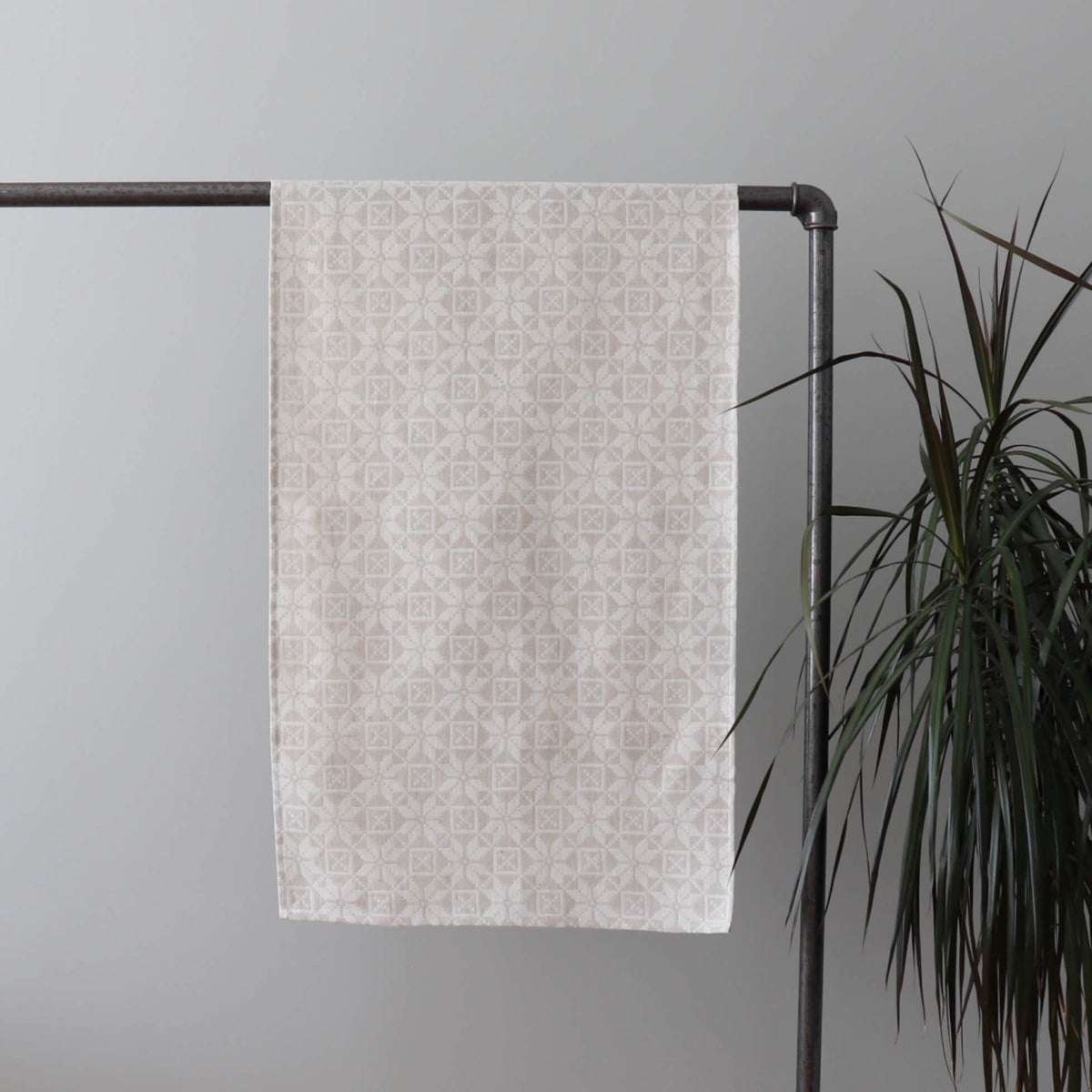 2. Beige table runner with kaheksakanna pattern hanging on metal rack, indoor plant beside