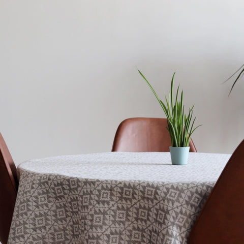 1. Round table with LOKO Harjumaa tablecloth featuring traditional mitten pattern, surrounded by brown chairs, with a green plant in a blue pot
