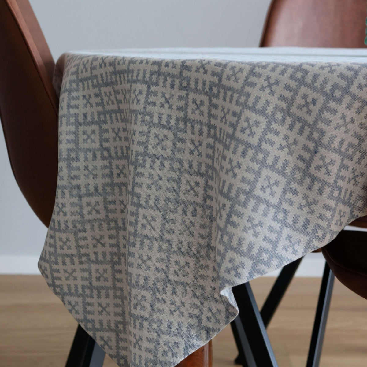 2. Close-up of LOKO Setumaa tablecloth draped over table edge, showcasing intricate mitten pattern in grey and white, with brown chair legs visible