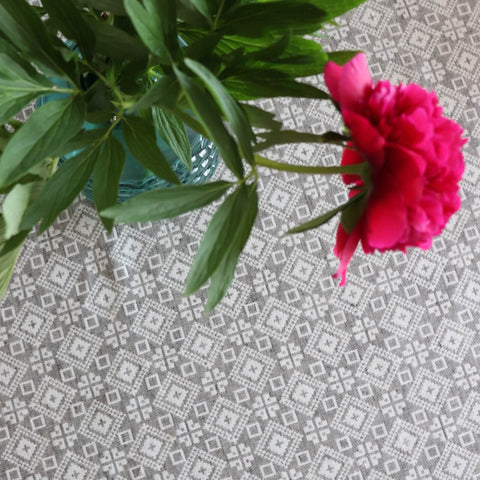 3. Overhead view of LOKO Tartumaa tablecloth displaying Kodavere folk art pattern, with a focus on the intricate design and a red flower in a blue vase
