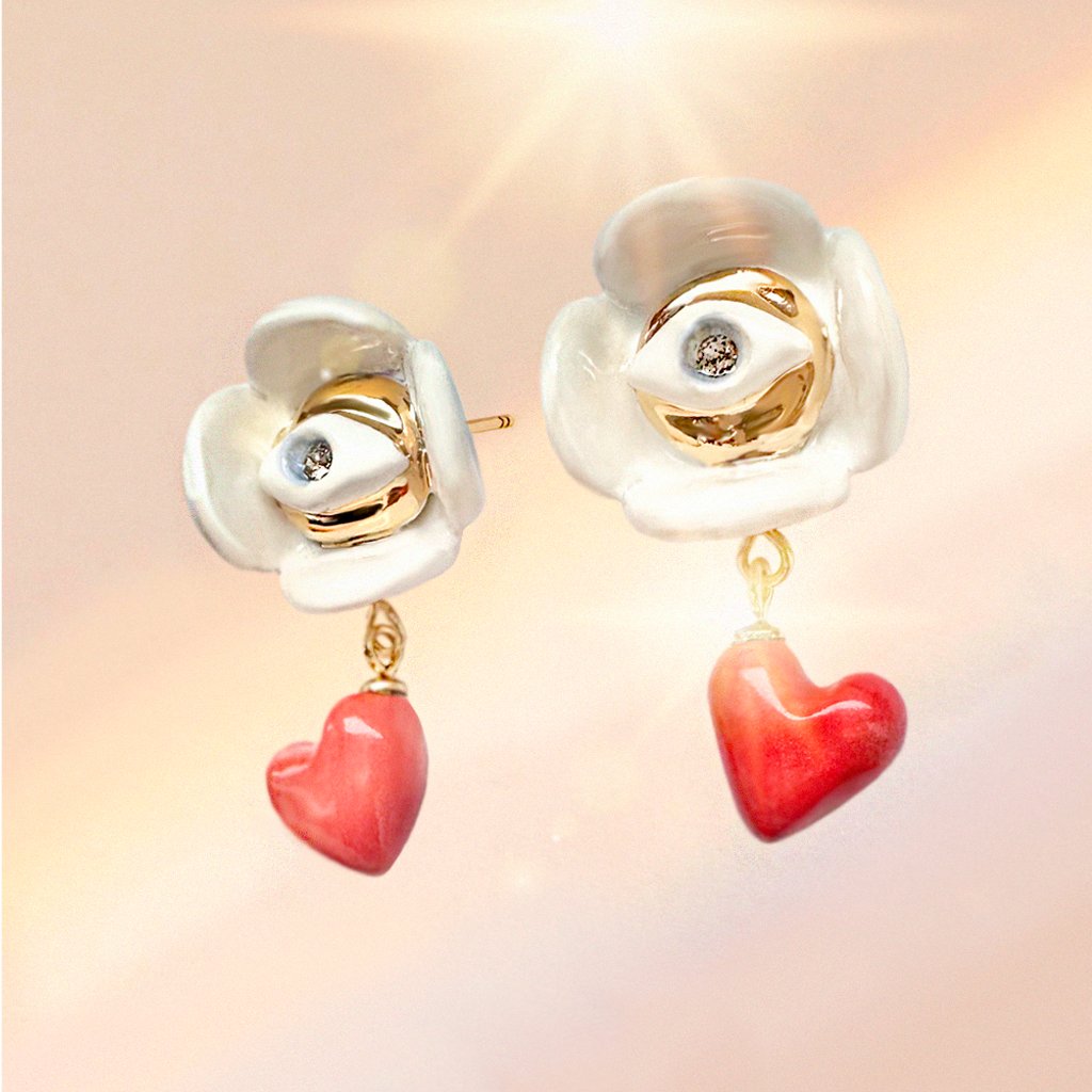 1. Lifestyle image of SCULP Love Is… earrings with Eye of Protection charm, featuring red heart dangles and Swarovski crystals, shown in a sunlit setting