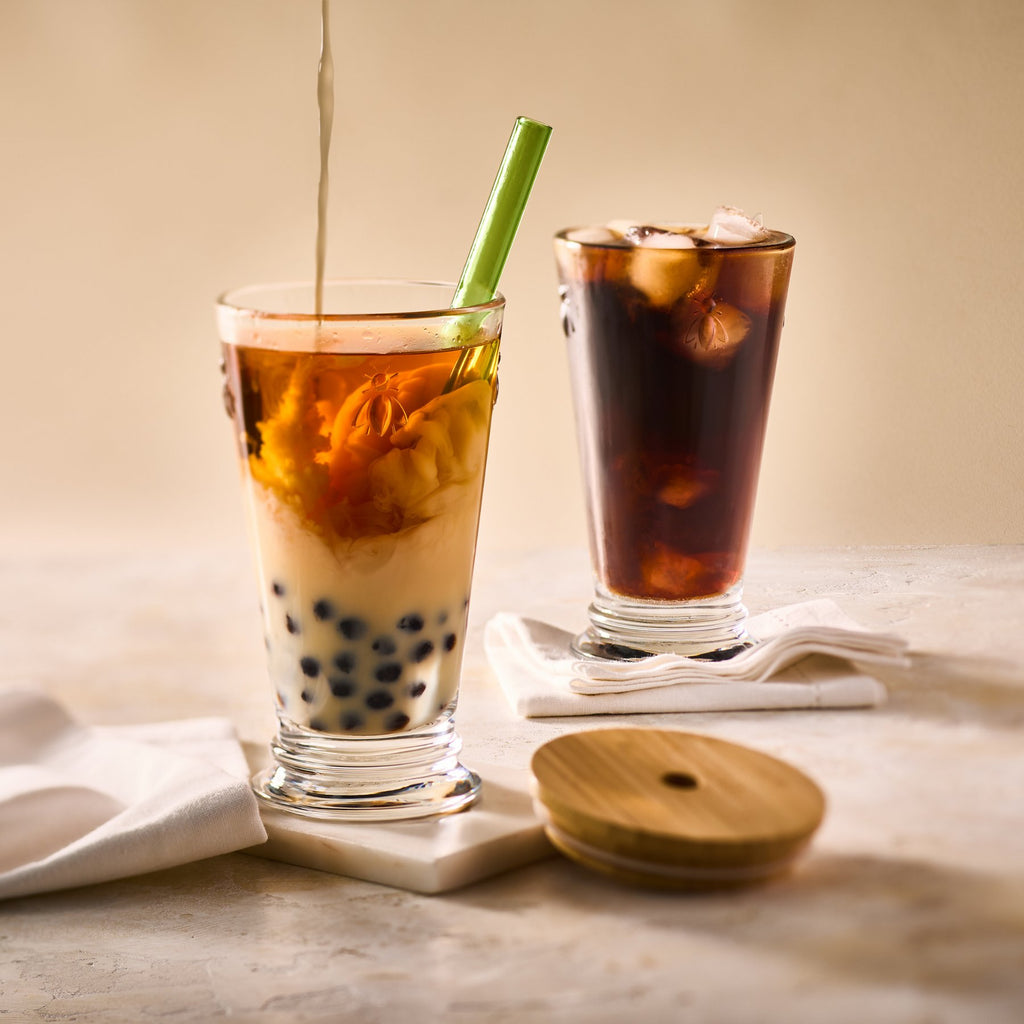 1. Two La Rochère Bee Smoothie Glasses filled with bubble tea and iced coffee on a marble surface, with bamboo lid and green straw, creating a stylish drink presentation