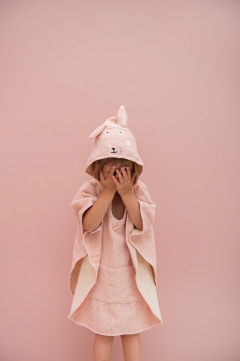 3. Child standing in pink hooded bathing poncho with rabbit design, hands covering face against pink background