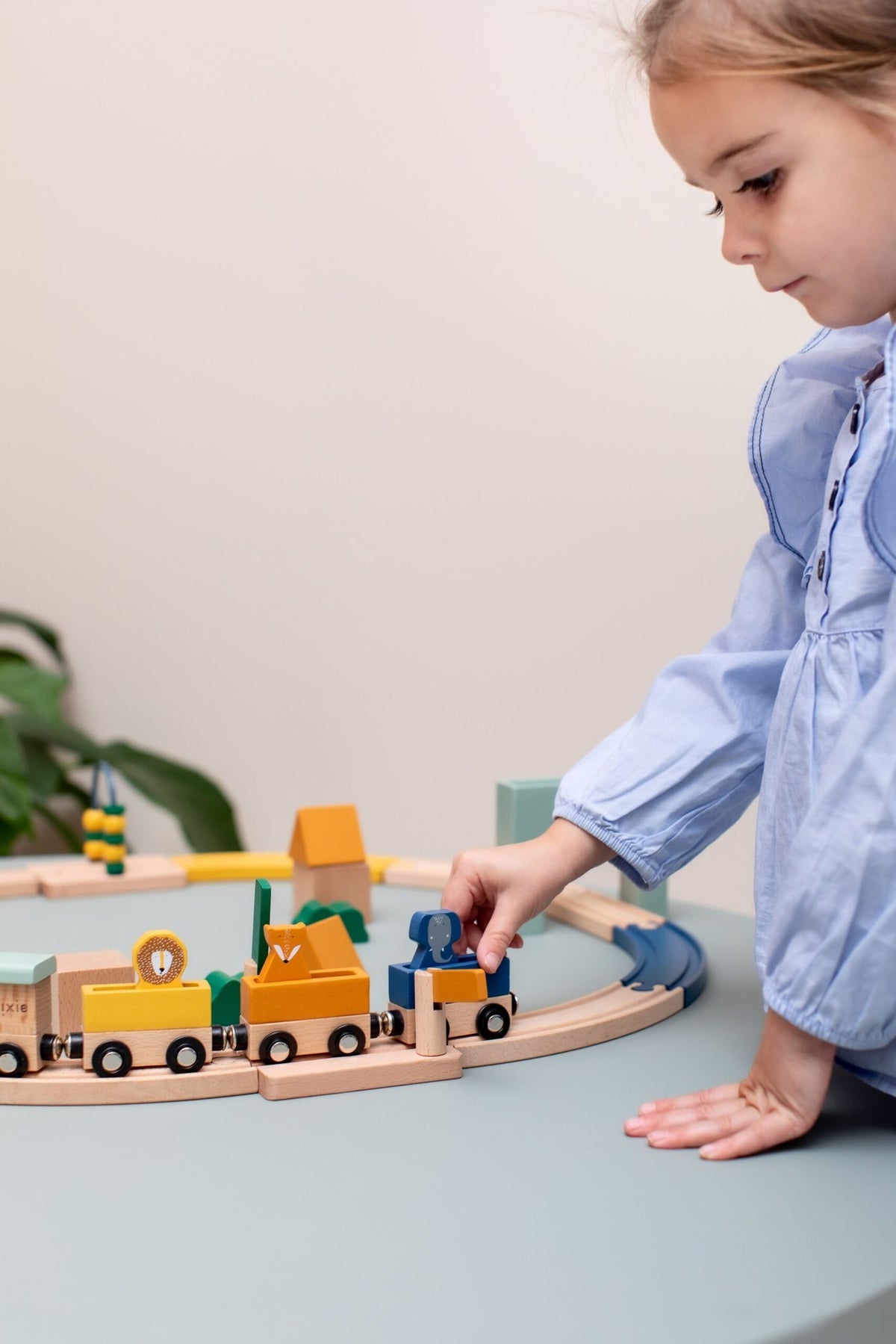 1. Child playing with Trixie Baby Wooden Railway Set on a table, wearing a blue shirt