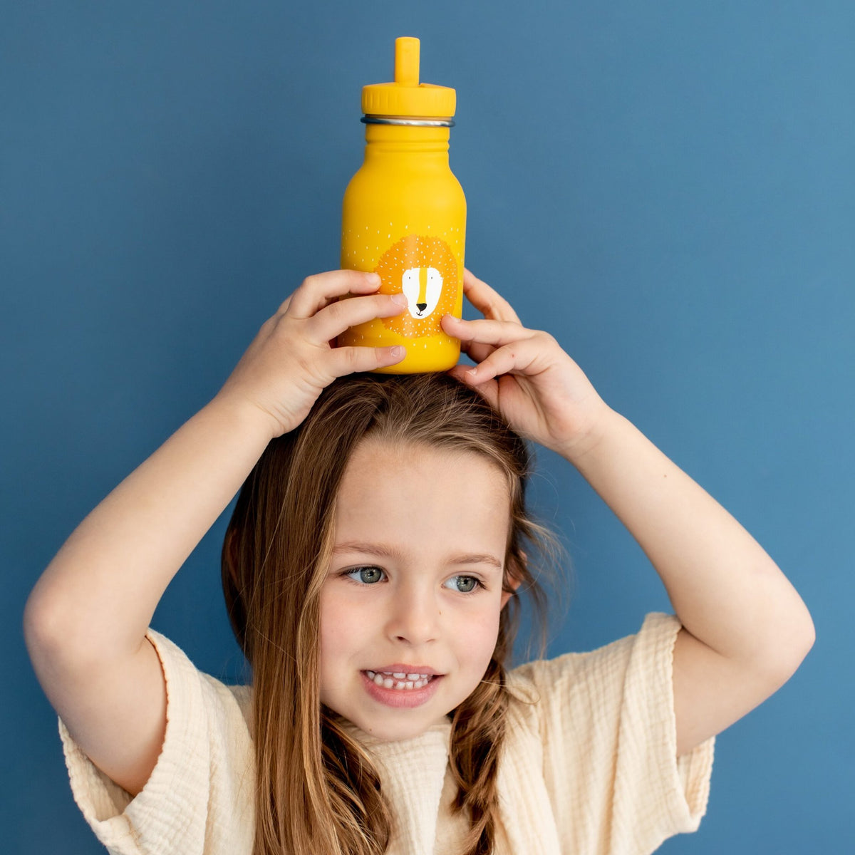 1. Child holding yellow stainless steel bottle with lion face design on head against blue background