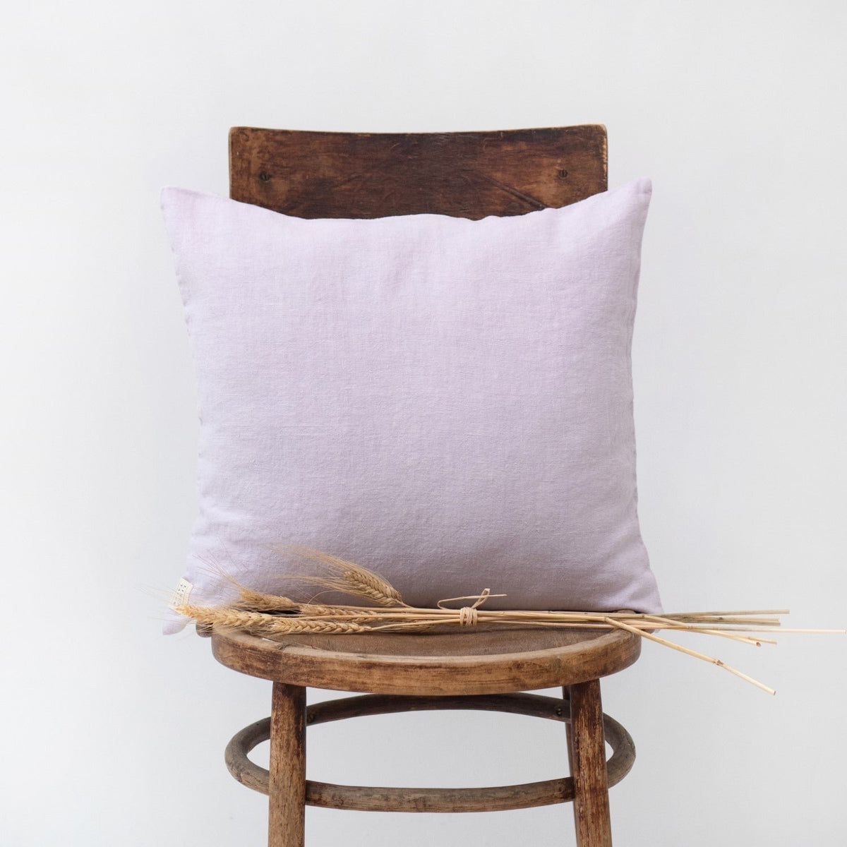 8. Lavender fog Linen Tales cushion cover on a wooden chair with dried wheat stems
