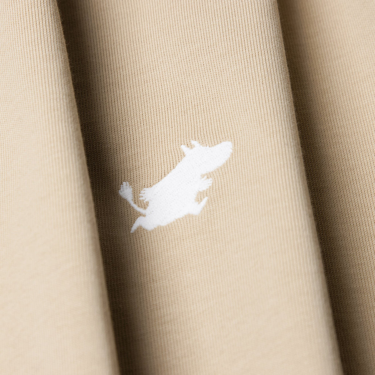6. Close-up of white Moomin logo on beige Moomin Classics heavy t-shirt fabric