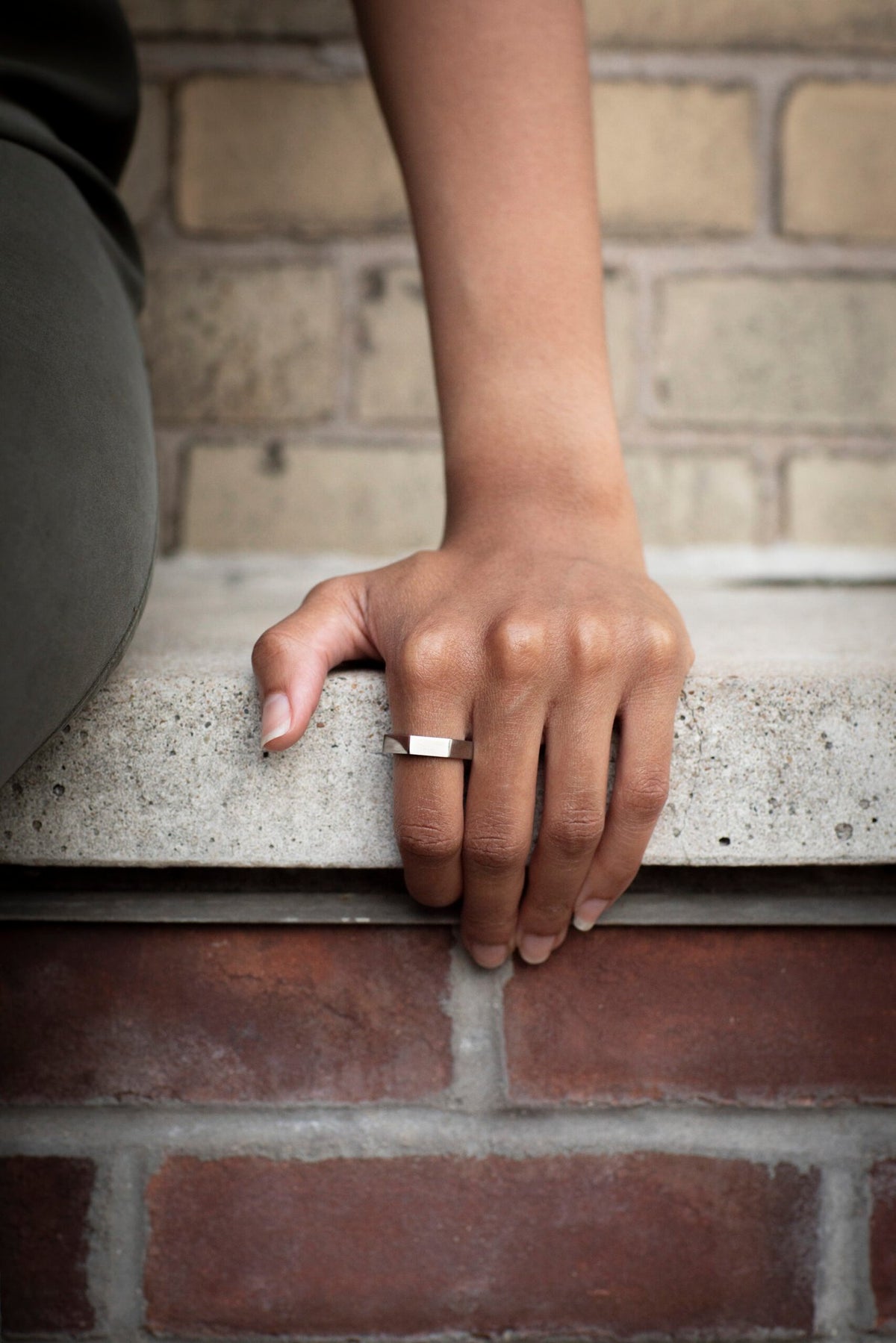 2. Close-up of woman's hand wearing Lentsius Plico ring in stainless steel against brick wall