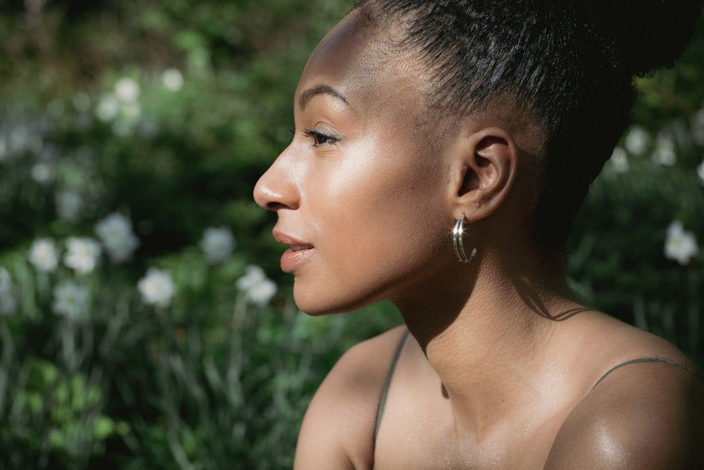 2. Side profile of woman wearing Lentsius Linea earrings in a garden setting, highlighting unique stainless steel design