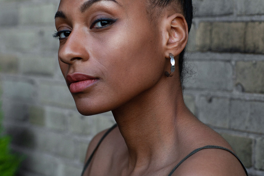 2. Close-up of woman wearing Lentsius Mare earrings against brick wall