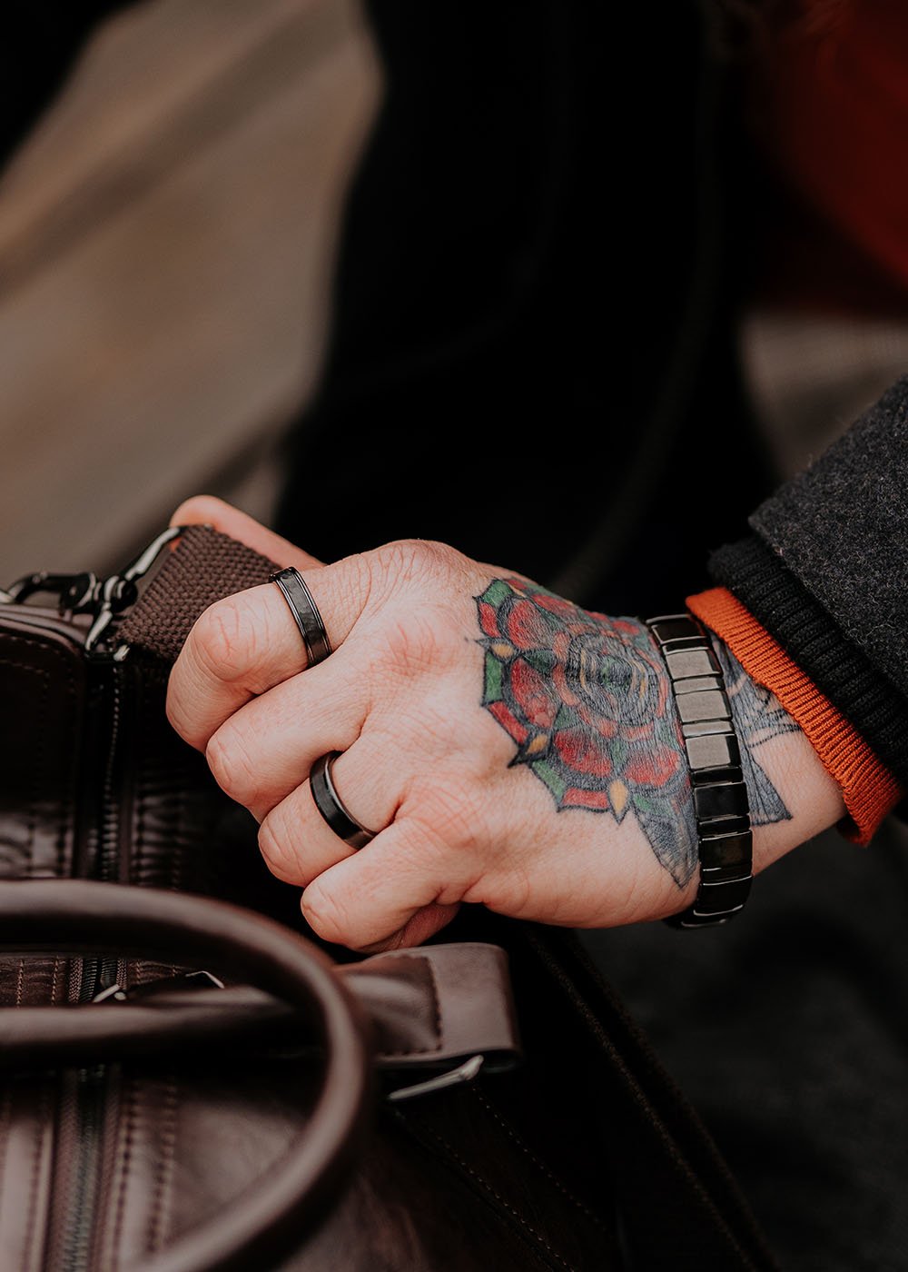 1. Man with tattooed hand wearing Leomani Bonard black ceramic bracelet holding a brown leather bag