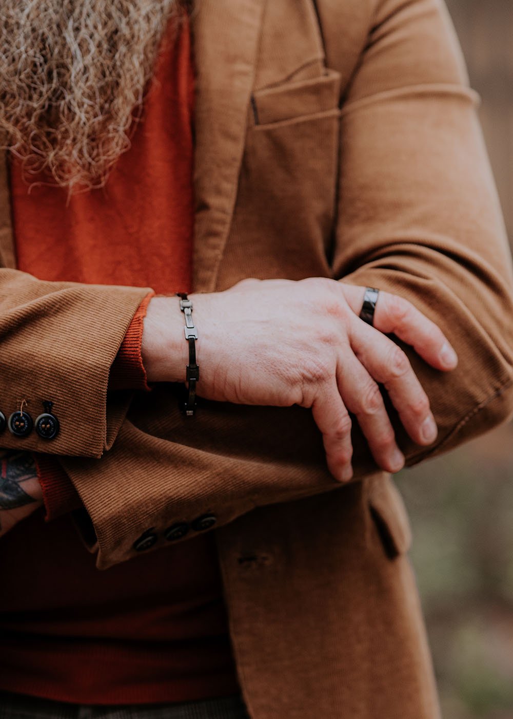 1. Man wearing Leomani Cody black ceramic bracelet with brown jacket and red shirt, arms crossed outdoors
