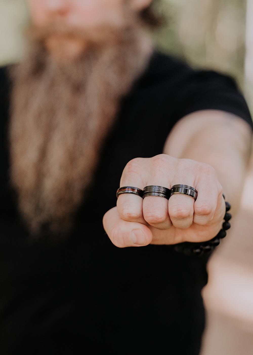 1. Man wearing three black ceramic rings with natural veneer, focus on hand in outdoor setting