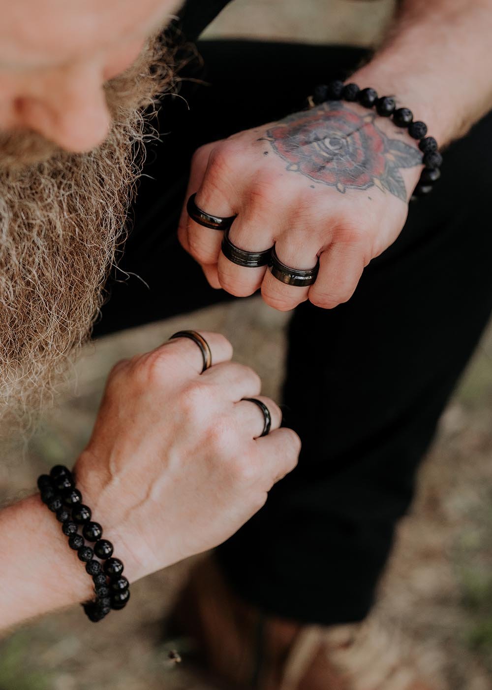 1. Two men wearing black ceramic rings and bracelets outdoors, one with a tattooed hand