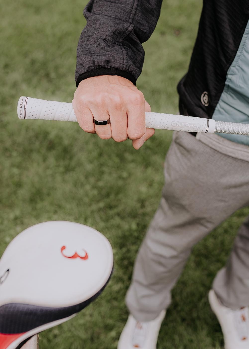 1. Man wearing Leomani black ceramic ring while holding a golf club on a grassy field