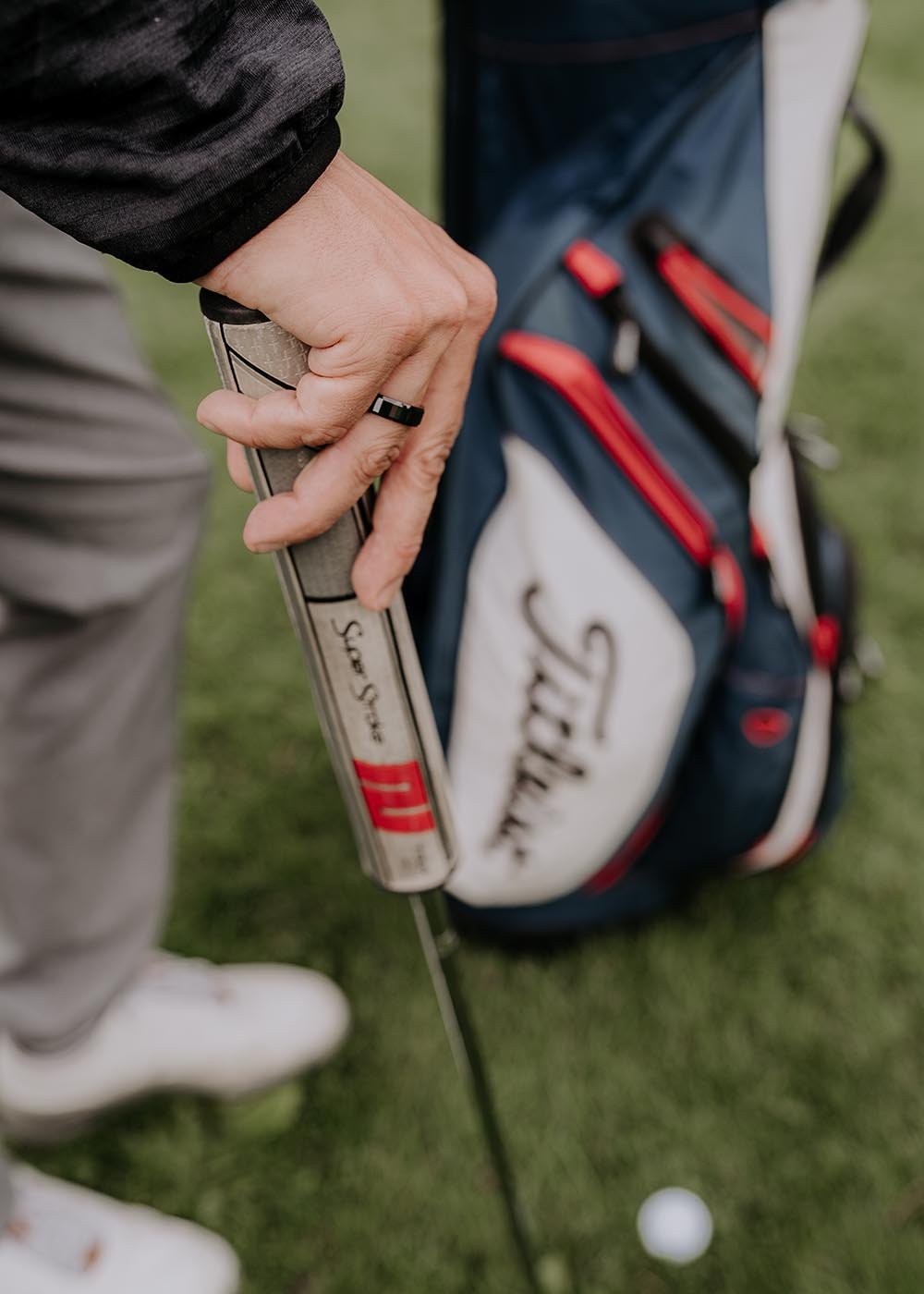 1. Man wearing Leomani black ceramic ring holding a golf club on a grassy field with golf bag in background