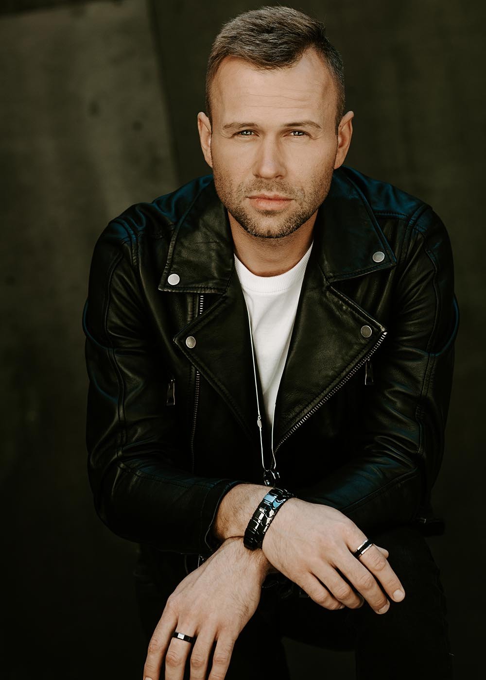 1. Man in leather jacket wearing Leomani men's stainless steel rings and bracelet, seated pose