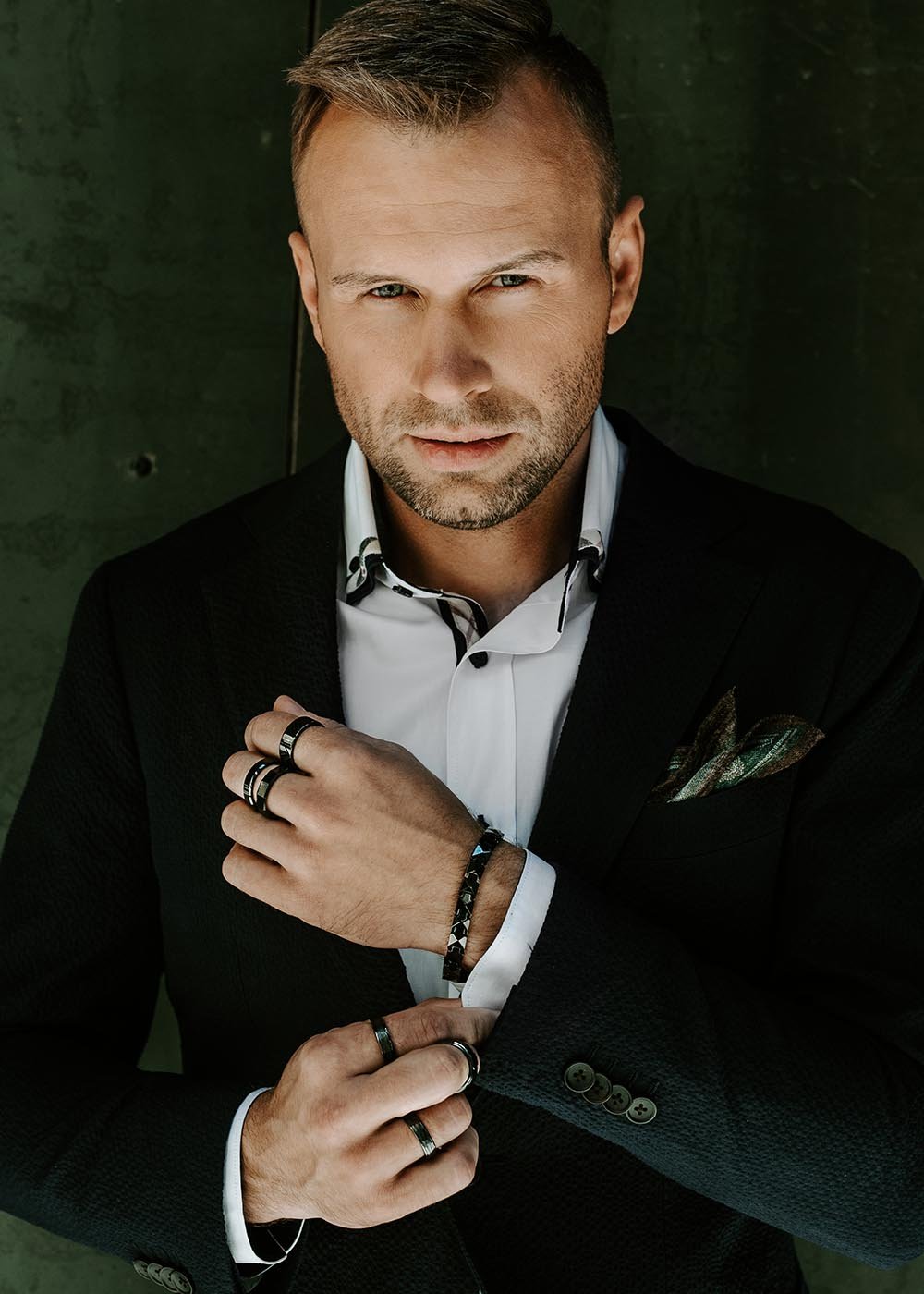 1. Man wearing Leomani Genf black ceramic bracelet with stainless steel clasp, styled with a black suit and white shirt, standing against a dark textured background