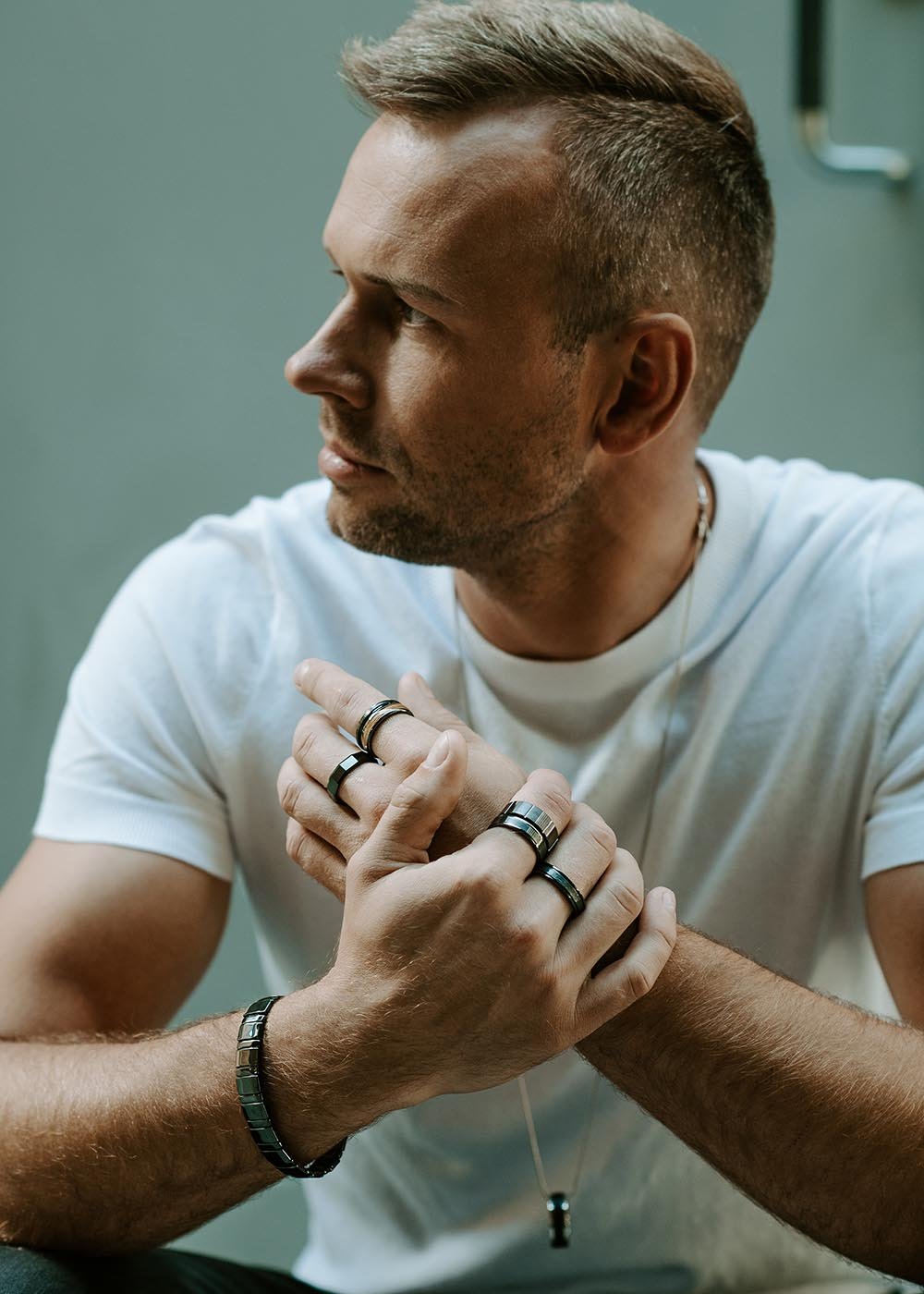 3. Man wearing multiple Leomani rings and bracelet, sitting casually in a white t-shirt