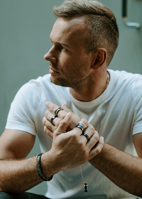 3. Man wearing multiple Leomani rings and bracelet, sitting casually in a white t-shirt