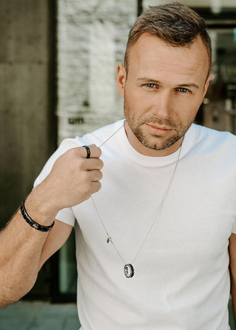 1. Man wearing Leomani black ceramic ring and bracelet, holding a necklace, in urban setting