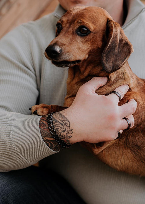 1. Man wearing Leomani Rocco black ceramic bracelet holding a small brown dog, showcasing tattooed arm and casual attire