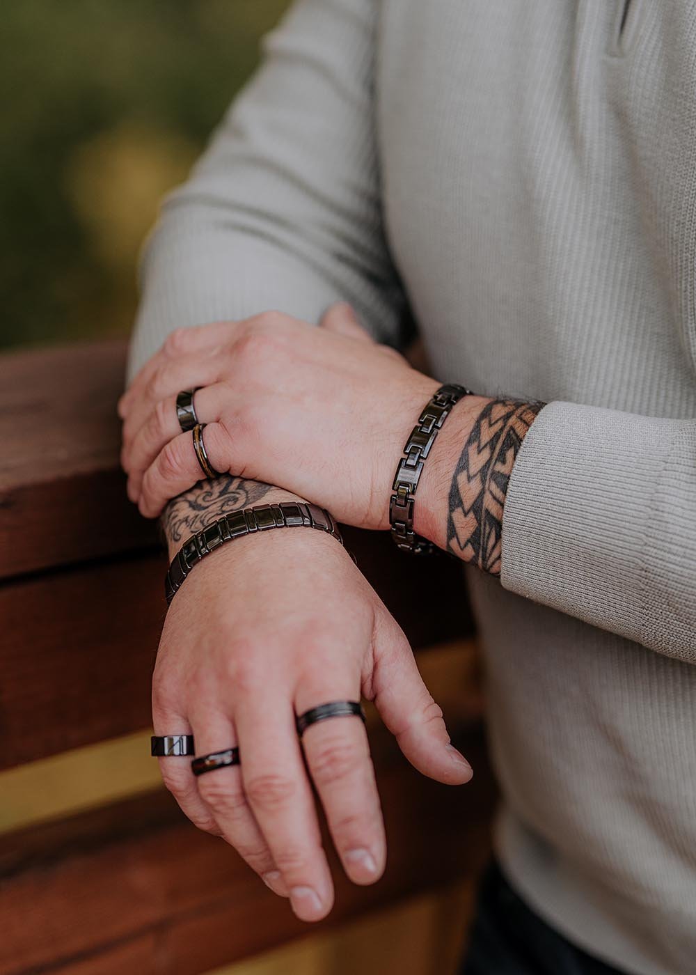 3. Close-up of man's hands wearing Leomani Trey black ceramic bracelet and rings, resting on wooden railing
